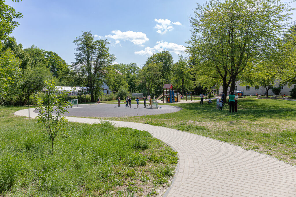 Gartenbild aus der Kita Kaulsdorf mit Blick auf den Rollerparcour und spielenden Kindern.