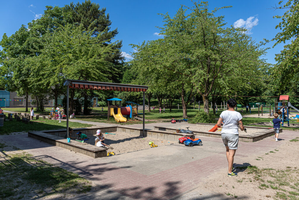 Kleinkinder spielen im Sandkasten, der große Garten der Kita Kaulsdorf zeigt vielfältige Spielmöglichkeiten.