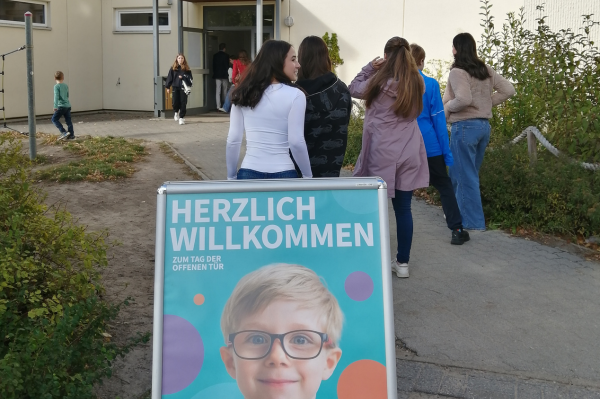 Schülergruppe 6. Klasse auf dem Weg ins Freizeitgebäude der BEST-Sabel Grundschule Kaulsdorf, im Vordergrund ein Aufsteller "Herzlich Willkommen"
