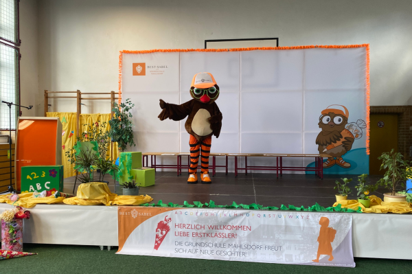 BEST-Sabel Maskottchen Gutav, eine Eule, steht auf der Bühne in der Turnhalle, die für die Einschulungsfeier dekoriert ist und die Erstklässler willkommen heißt