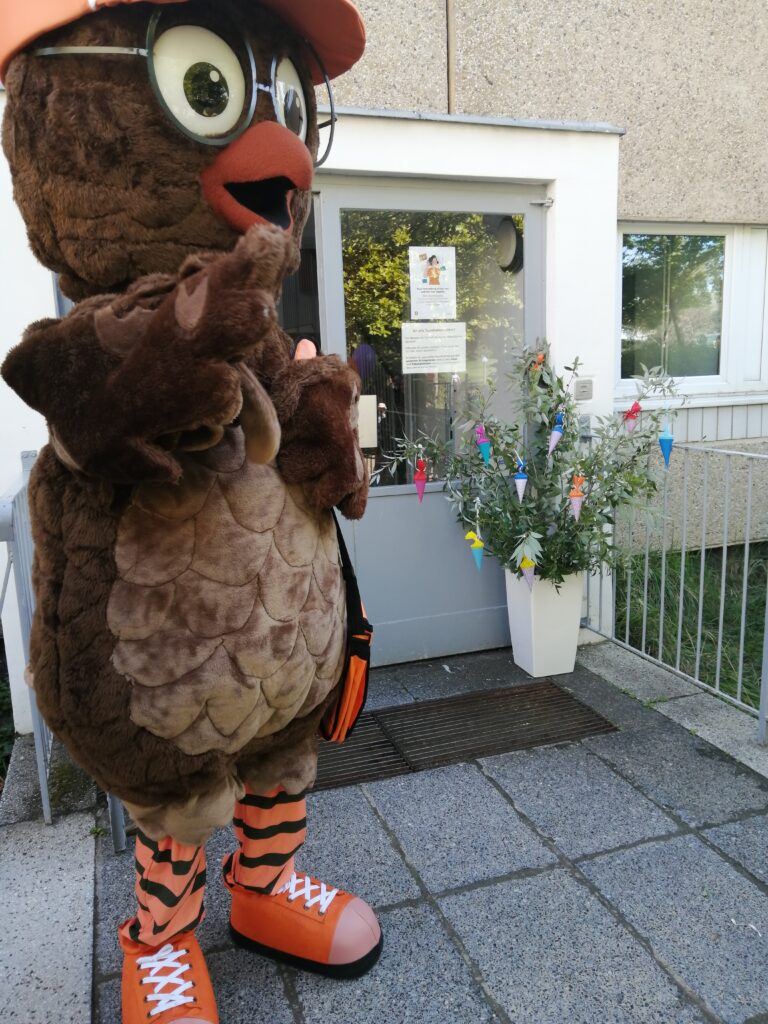 Lebensgroßes BEST-Sabel Maskottchen Gustav, eine Eule, winkt vor dem dekorierten Eingang der Turnhalle den Neuankömmlingen zu